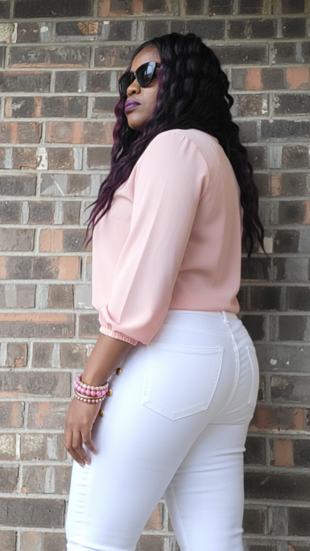 Model wearing a pink blouse, white skinny jeans, and pink and gold bracelets