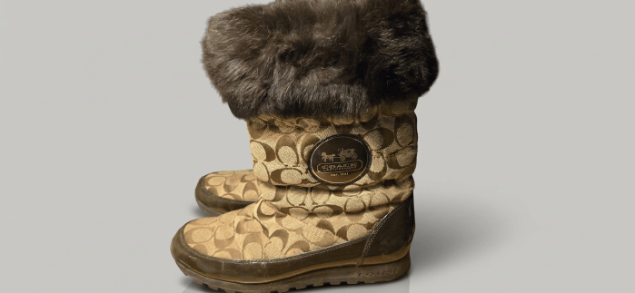 Pair of Coach boots with brown signature pattern, dark rubber soles, and fur cuffs.