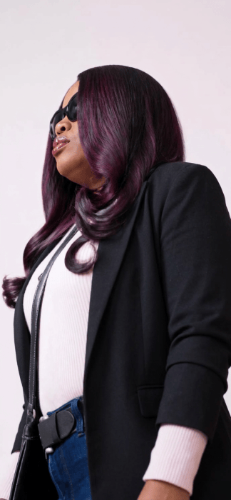 Woman wearing sunglasses, a black blazer, white sweater, and purple-tinted hair