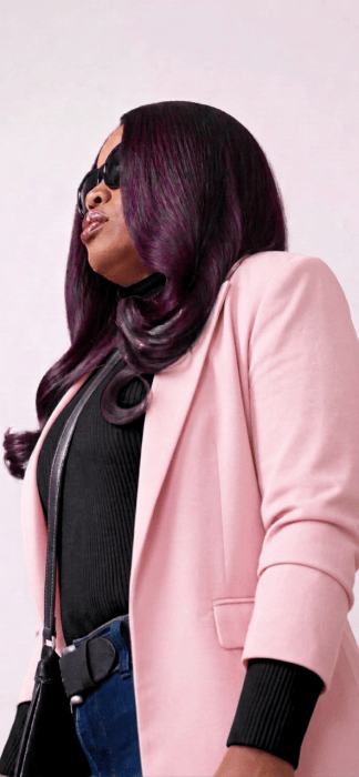 Person wearing sunglasses, a pink blazer, and long purple hair